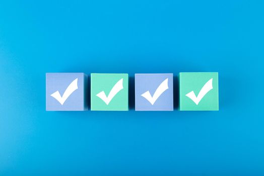 Four checkmarks on multicolored cubes in a row on blue background with copy space. Concept of questionary, checklist, to do list, planning, business or verification. Modern minimal composition 