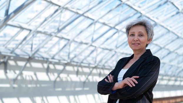 Happy successful mature Asian businesswoman posing with arms folded in the business building