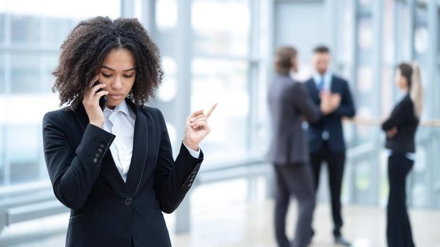 Black business woman talking on phone in office building, coworkers on background