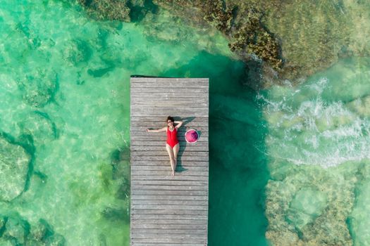 Top view of woman lying down on wooden pier at sunny summer day in Cancun, Mexico. Young sexy woman in the red swimwear in Caribbean. Summer beach vacation concept