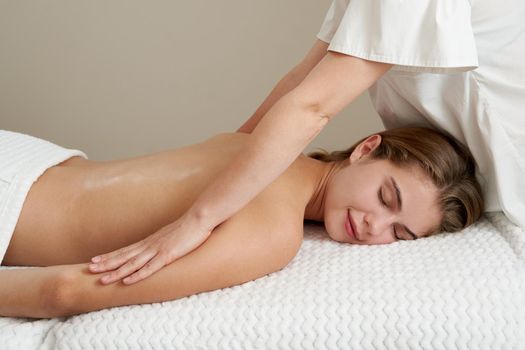 Masseur massaging young woman on massage table in a spa salon. Young woman relaxing during back massage at the spa. Spa treatment concept