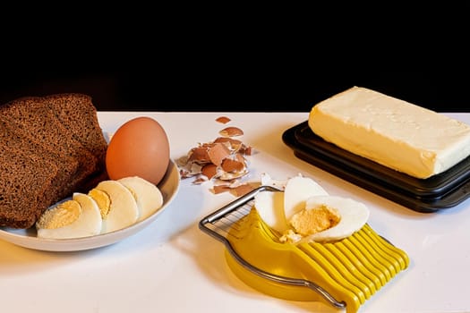 Making a breakfast sandwich, bread and butter and egg with egg on the table. Black background, close up