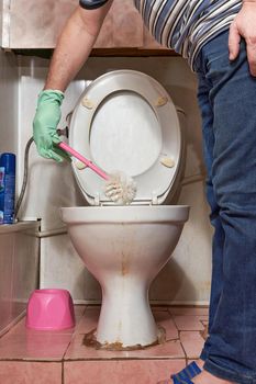 Hand with toilet brush cleans old dirty toilet bowl. Cleaning the toilet with household gloves