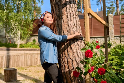 Middle aged woman hugging a tree, energy of nature. Relaxation, mental health, rest, freedom, mature people concept