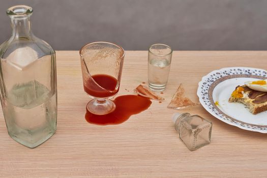 A broken glass and red tomato juice spilled on the table next to a bottle of vodka. Concept drunkenness and alcoholism