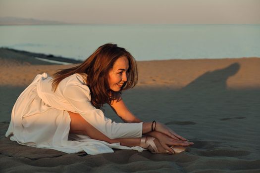 A girl in a fly white dress dances and poses in the sand desert at sunset.