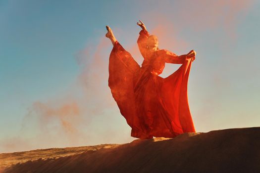 Woman in red dress dancing in the desert at blue sky