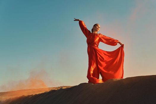 Woman in red dress dancing in the desert at blue sky