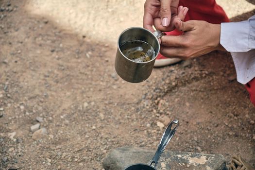 Hands of an adult man pouring hot coffee from a turk into a metal mug