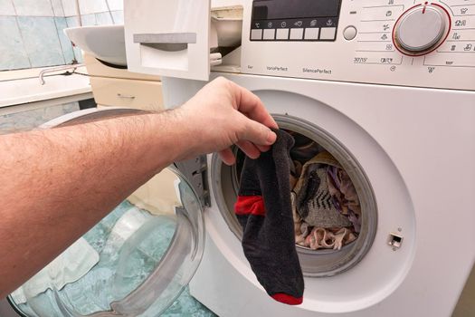 A hand holds a clean black sock in front of an open washing machine. Washing clothes in a washing machine