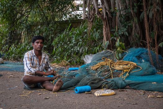 Indian Fisherman repairs fishing net in Goa, India