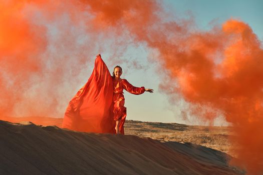 Woman in red dress dancing in the desert at blue sky