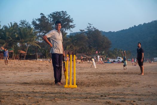 Group of Indian adults playing cricket on beach at sunset, Goa, India