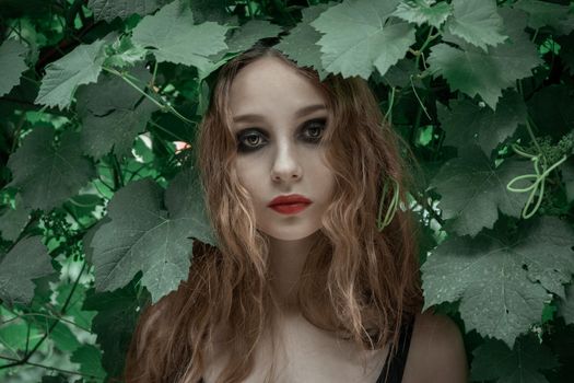 Portrait of beautiful young woman with red lips staying in front of green leaves