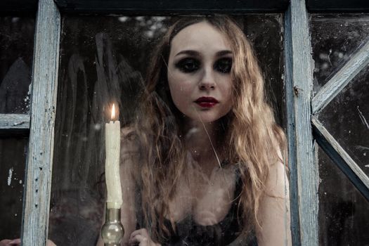 Beautiful sad young girl looking out the window with a candle, good for book cover