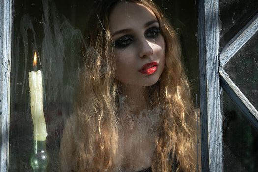 Beautiful sad young girl looking out the window with a candle, good for book cover