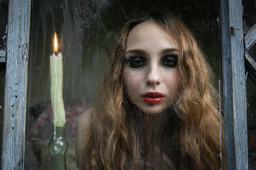 Beautiful sad young girl looking out the window with a candle, good for book cover