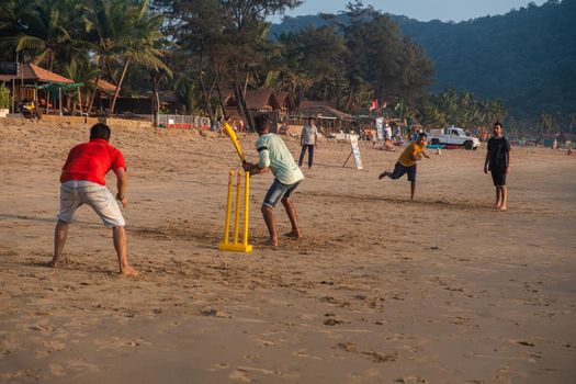 Group of Indian adults playing cricket on beach at sunset, Goa, India