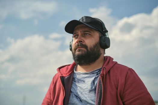 Middle-aged European man in headphones outdoors listening to music against the background of the sky
