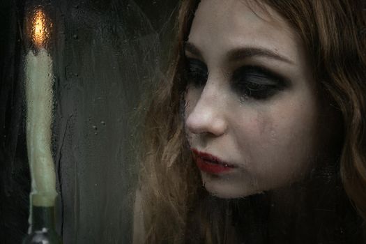 Beautiful sad young girl looking out the window with a candle, good for book cover