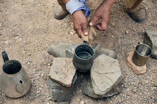 Hands of an adult man pouring hot coffee from a turk into a metal mug