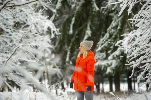 A girl in a red jacket walks through a snowy forest in winter.