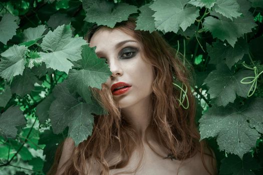 Portrait of beautiful young woman with red lips staying in front of green leaves