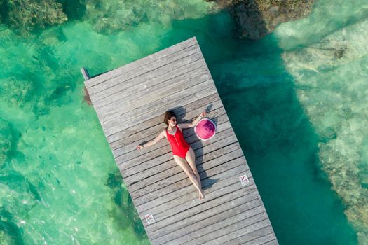 Aerial view of woman laying on wooden pier at sunny summer day in Cancun, Mexico, top view. Young sexy woman in red swimsuit in summertime in Caribbean. Summer beach vacation concept