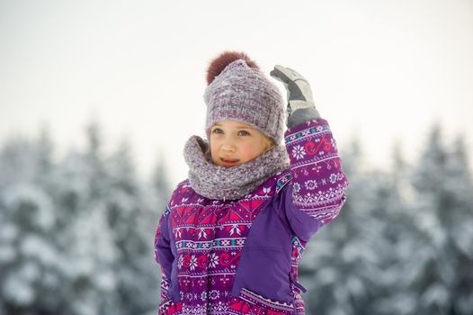 a little girl in winter in purple clothes walks through a snow-covered forest.