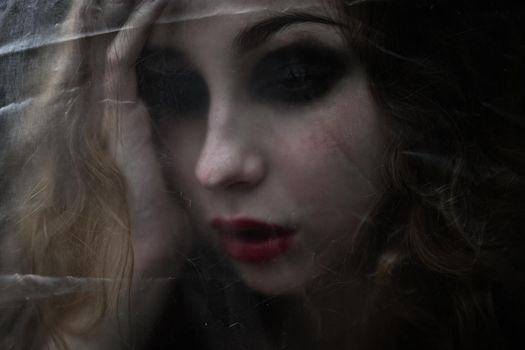 Young beauty sad woman trapped behind a plastic sheet as protection against COVID-19. Nicely fits for book cover