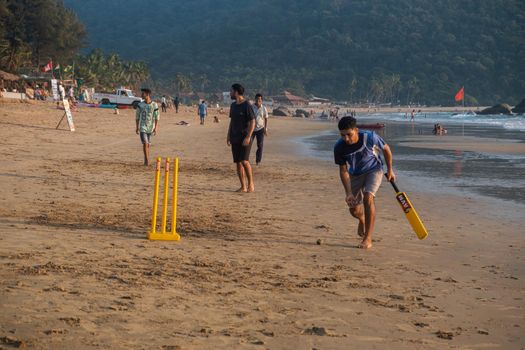 Group of Indian adults playing cricket on beach at sunset, Goa, India