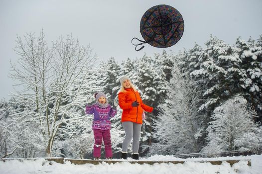 Family mom and daughter in winter with an inflatable circle walk through the snow-covered forest.