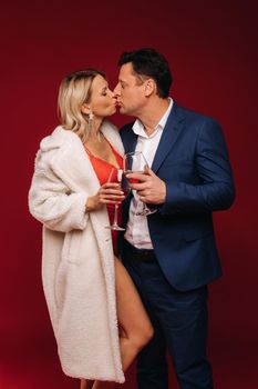 A man and a woman in love with a glass of champagne on a red background kiss.