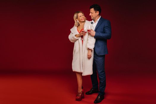 A man and a woman in love with a glass of champagne on a red background embrace.