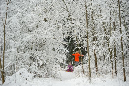 Family mom and daughter in winter with an inflatable circle walk through the snow-covered forest.