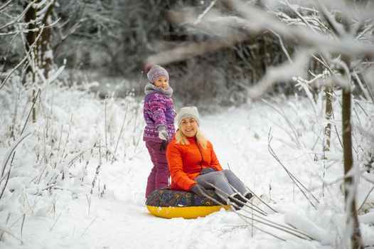 Family mom and daughter in winter with an inflatable circle walk through the snow-covered forest.