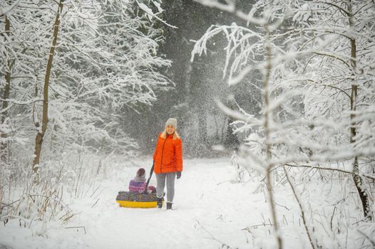 Family mom and daughter in winter with an inflatable circle walk through the snow-covered forest.