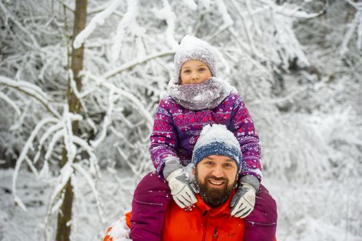 Family dad and daughter walk in the snow-covered forest in winter.