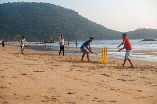 Group of Indian adults playing cricket on beach at sunset, Goa, India