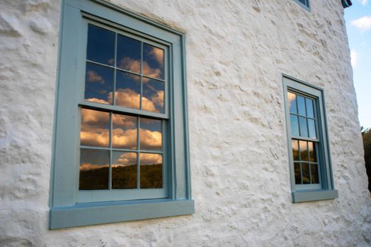 Beautiful whitewashed stone colonial American Pennsylvania home with blue window frames and antique twelve-pane glass. Blue sky and golden hour clouds are reflected.