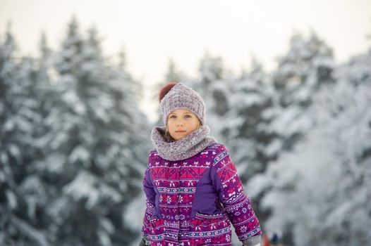 a little girl in winter in purple clothes walks through a snow-covered forest.