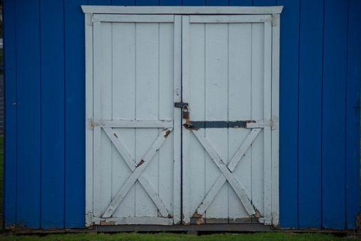 Close up of wooden frame back yard shed and two closed wooden doors with lock. Blue and white colors are bright in natural light, no people, with copy space