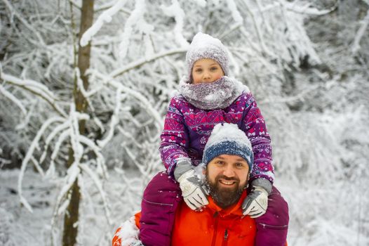 Family dad and daughter walk in the snow-covered forest in winter.