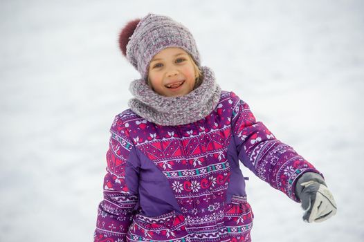 a little girl in winter in purple clothes walks through a snow-covered forest.