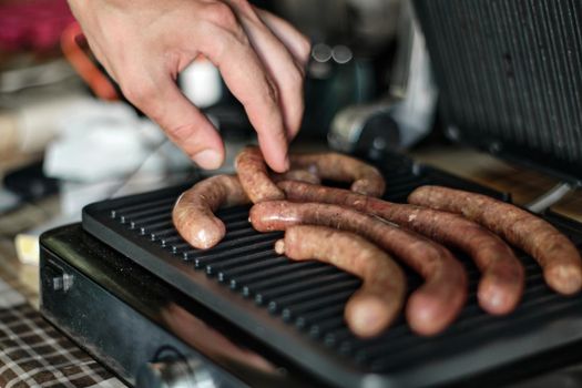 Man's hand lays out raw sausages on the grill, close up shot