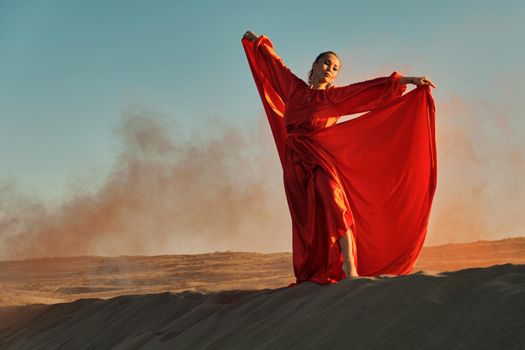 Woman in red dress dancing in the desert at blue sky