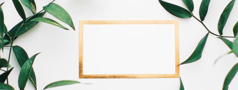 Blank white and gold card, green leaves on white background as botanical frame flatlay, wedding invitation and branding, flat lay design concept