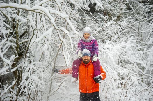 Family dad and daughter walk in the snow-covered forest in winter.