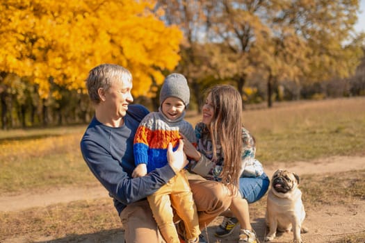 A young family with a small child and a dog spend time together for a walk in the autumn park.