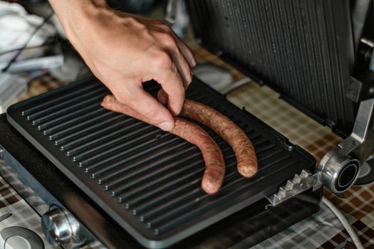Man's hand lays out raw sausages on the grill, close up shot